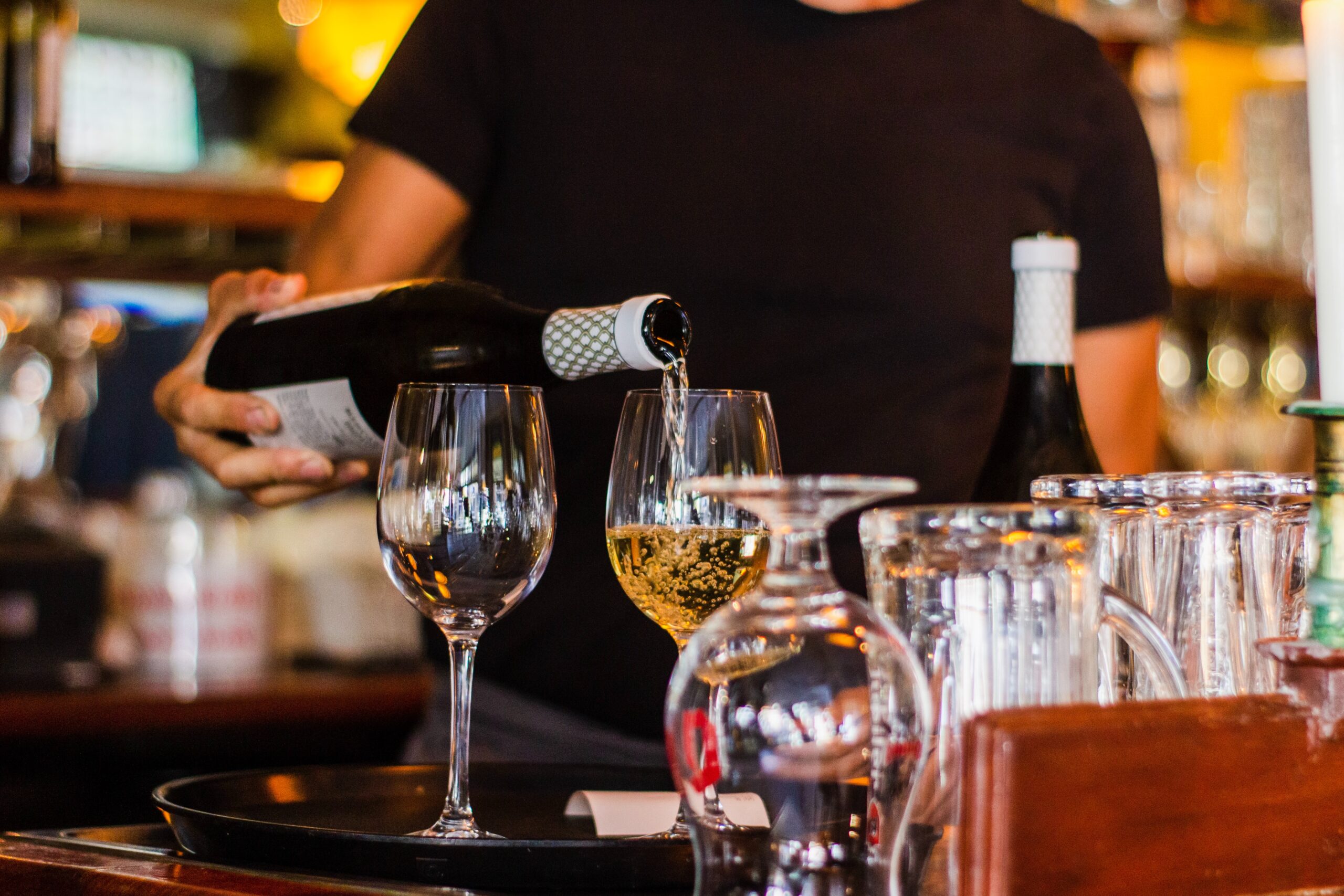 Bild på en bar där någon häller upp vin i vinglas