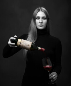Porträttbild på Sara Bernhardsson i svartvitt med vinflaska i färg