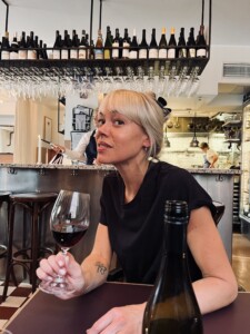 Porträttbild på Ninna Prage med vinglas i handen sittandes i en vinbar