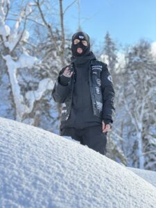 Porträttbild på snowboardproffset PJ Gustafsson i sin klassiska utstyrsel med skinnpaj och balaklava, i snölandskap.
