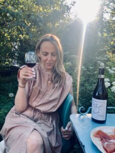 Bild på Jonna Berg som dricker vin i en berså med sol i bakgrunden