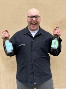 Porträttbild på skrattande David Favaro med två flaskor i händerna 