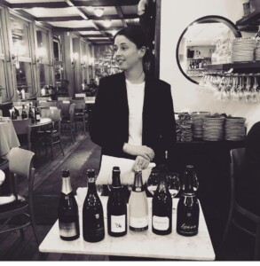 Porträttbild på Frida WInters framför vinflaskor i en restaurang